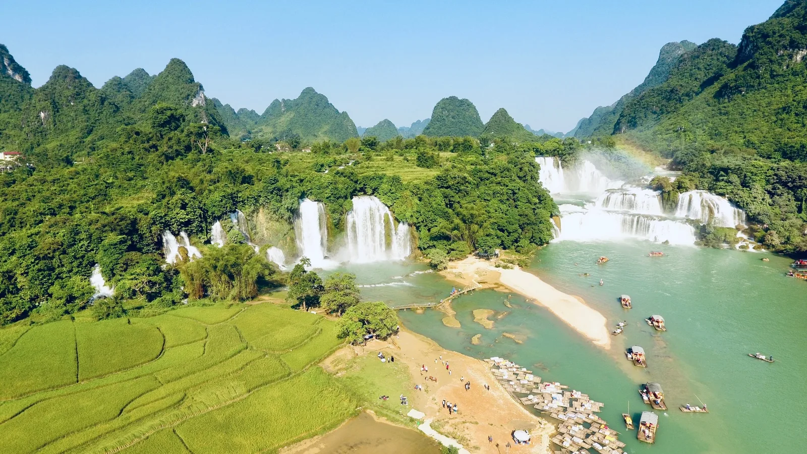 Toàn cảnh trên cao thác Bản Giốc đổ giữa núi đá vôi với thuyền du lịch và ruộng lúa xanh ở Cao Bằng