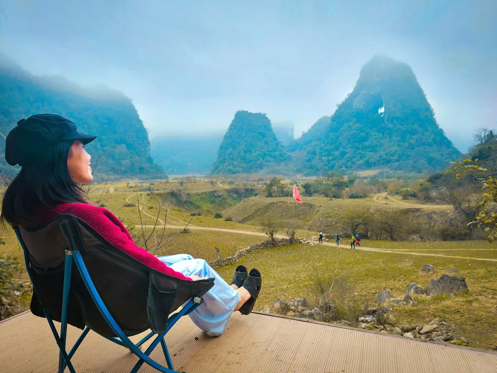 Một phụ nữ ngồi trên ghế cắm trại ngắm những ngọn núi đá vôi mờ sương và cánh đồng xanh ở Cao Bằng.